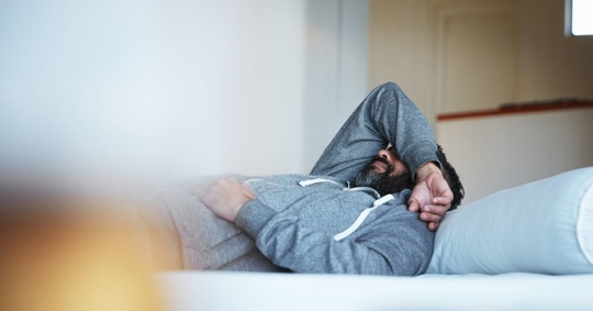 Selective focus photo of an individual laying in bed, with their arm over their eyes.
